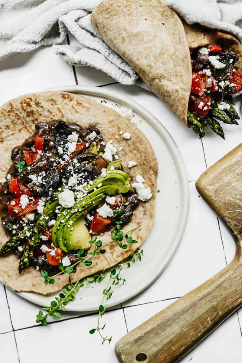 a tortilla filled with vegetables, avocado and vegan cheese