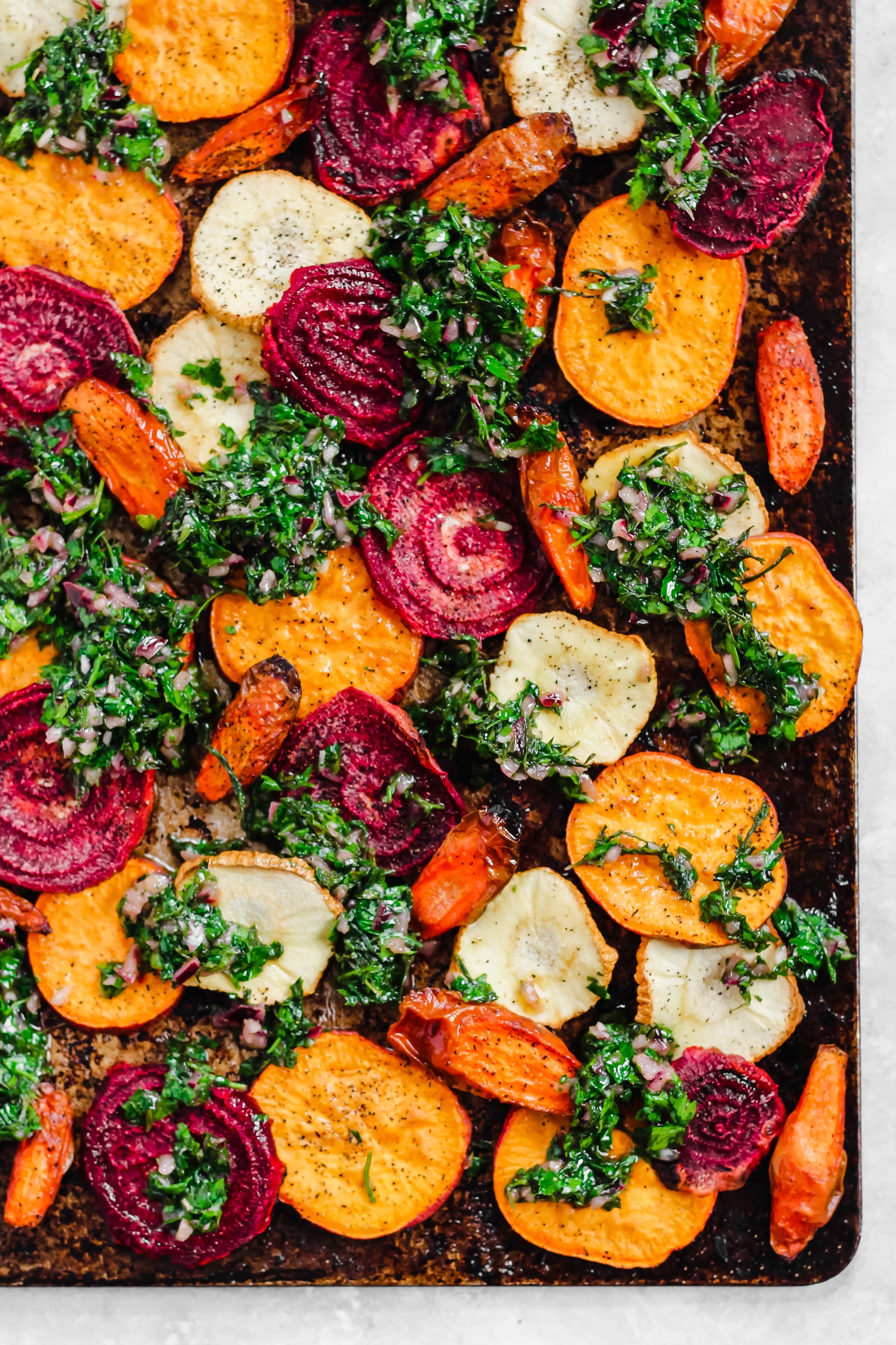 a sheet trap of sliced root vegetables topped with a carrot top chimichurri 